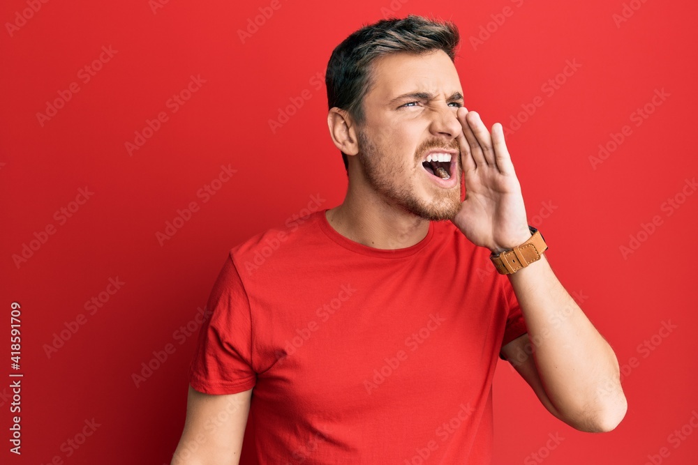 Handsome caucasian man wearing casual red tshirt shouting and screaming loud to side with hand on mouth. communication concept. Handsome caucasian man wearing casual red tshirt shouting and screaming loud to side with hand on mouth. communication concept.