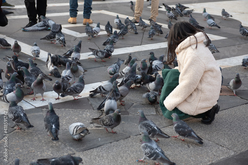 Little girl with long black hair with white fur sitting in the square with many doves.