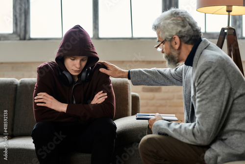 Psychotherapist touching shoulder of restless teenage boy