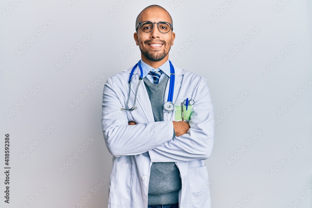 Hispanic adult man wearing doctor uniform and stethoscope happy face smiling with crossed arms looking at the camera. positive person. Hispanic adult man wearing doctor uniform and stethoscope happy face smiling with crossed arms looking at the camera. positive person.