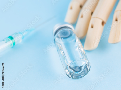 Vaccine, syringe and wooden human hand. Medical ampoule and syringe on blue background. Health care and disease prevention concept. Top view