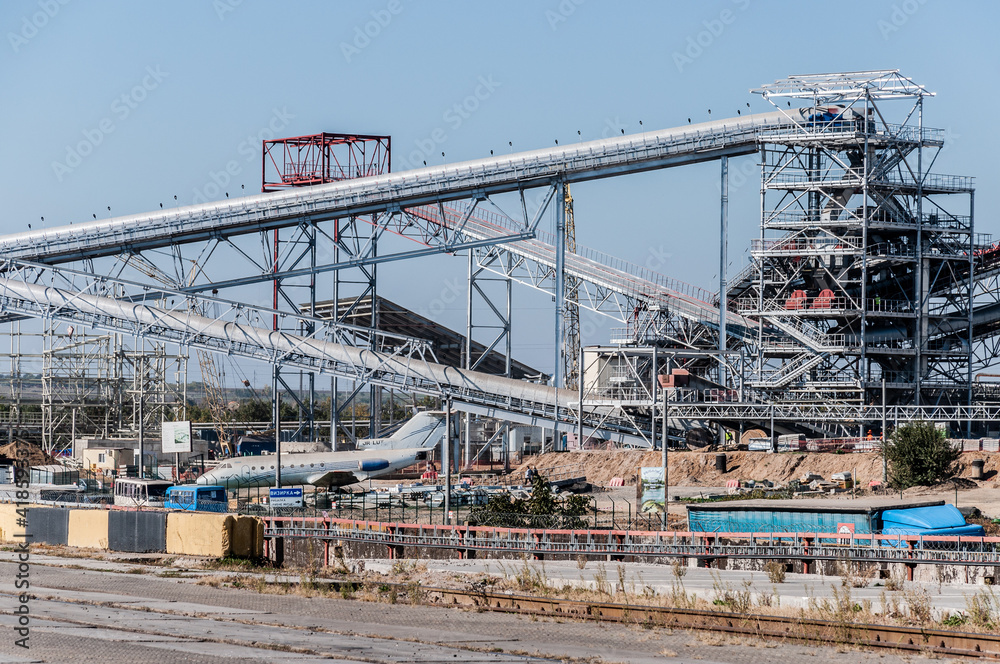 Grain cargo terminal of TIS Group, Ukraine largest dry cargo port. Grain transporter loader complex. Industrial metal pipeline construction and aircraft landed on ground.