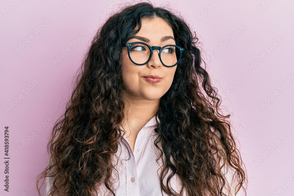 Obraz premium Young brunette woman with curly hair wearing casual clothes and glasses smiling looking to the side and staring away thinking.