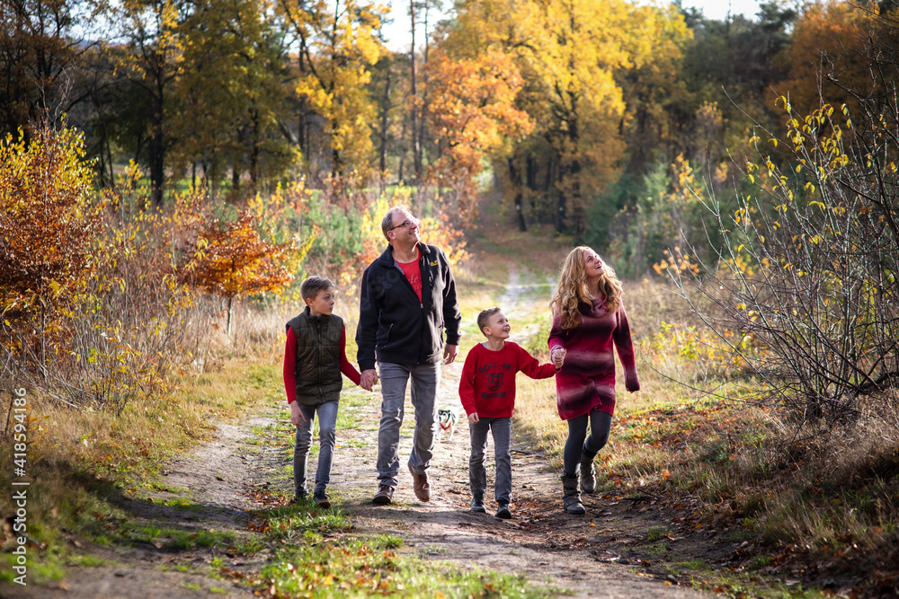 Eine glückliche, vierköpfige Familiegeht über dem langen Weg im Herbstwald und schauen sich um, Genießen die Natur und Herbstfarben