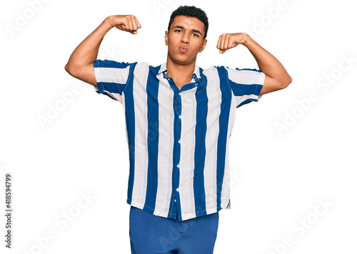 Young arab man wearing casual clothes showing arms muscles smiling proud. fitness concept.