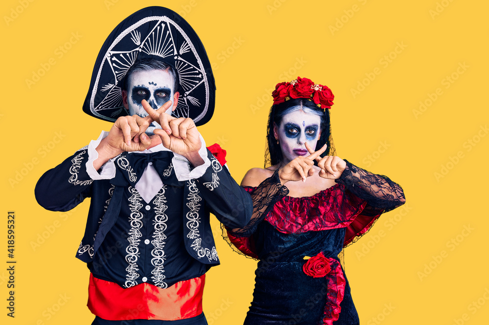 Young couple wearing mexican day of the dead costume over background rejection expression crossing fingers doing negative sign