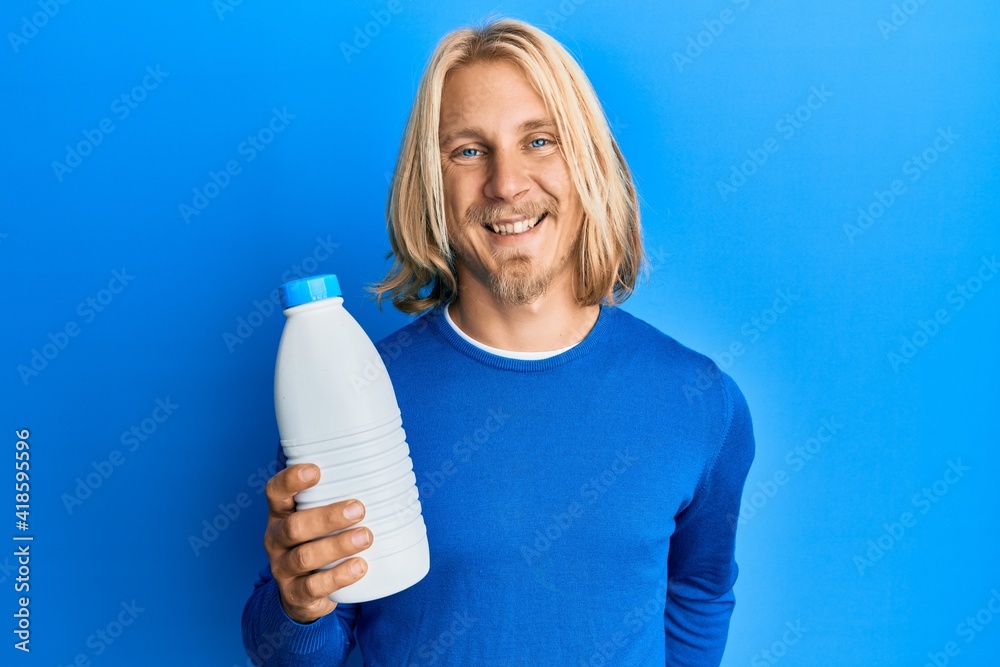 Caucasian young man with long hair holding liter bottle of milk looking  positive and happy standing and smiling with a confident smile showing  teeth Stock Photo | Adobe Stock