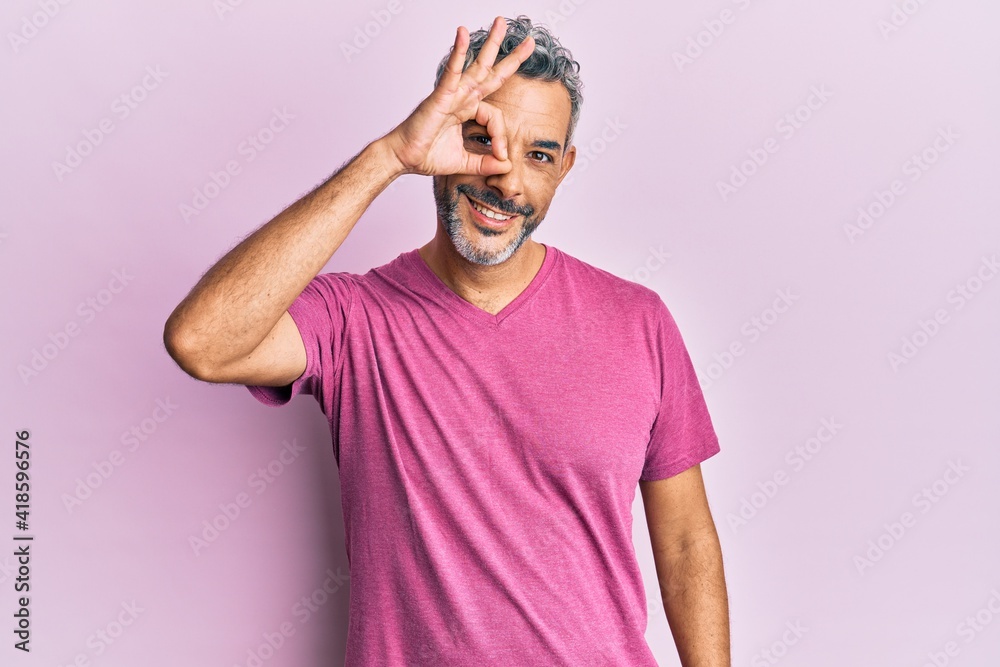 Middle age grey-haired man wearing casual clothes smiling happy doing ok sign with hand on eye looking through fingers Middle age grey-haired man wearing casual clothes smiling happy doing ok sign with hand on eye looking through fingers