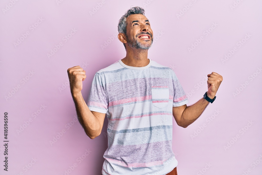 Middle age grey-haired man wearing casual clothes very happy and excited doing winner gesture with arms raised, smiling and screaming for success. celebration concept. Middle age grey-haired man wearing casual clothes very happy and excited doing winner gesture with arms raised, smiling and screaming for success. celebration concept.