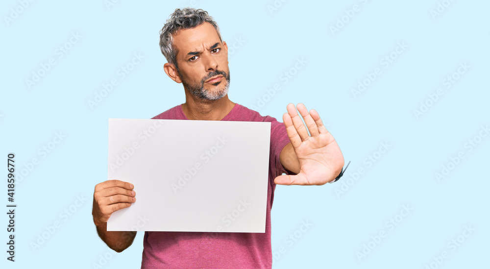 Middle age grey-haired man holding blank empty banner with open hand doing stop sign with serious and confident expression, defense gesture Middle age grey-haired man holding blank empty banner with open hand doing stop sign with serious and confident expression, defense gesture