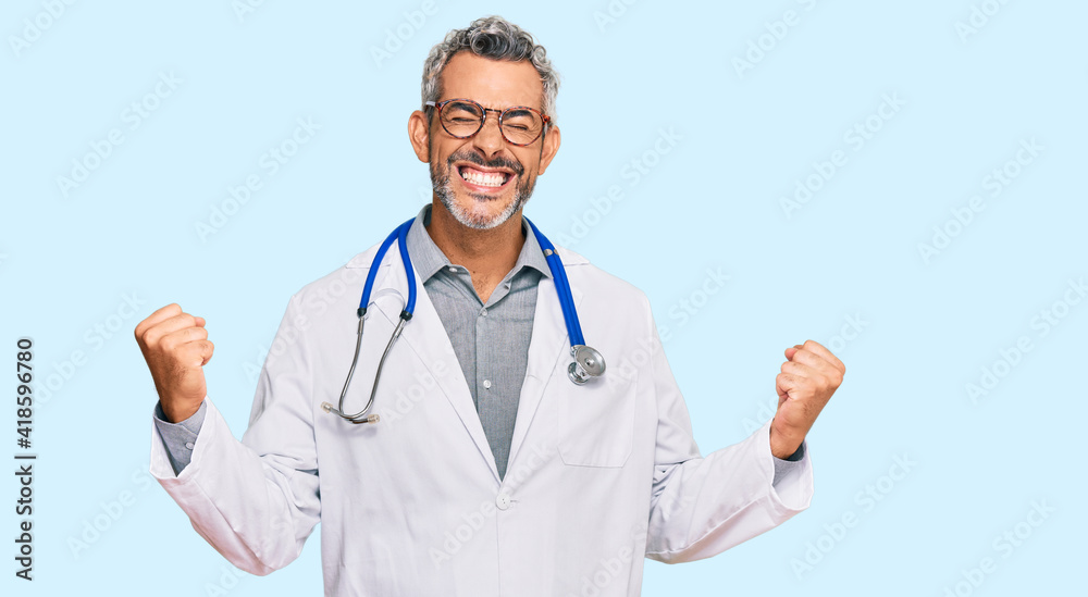 Middle age grey-haired man wearing doctor uniform and stethoscope very happy and excited doing winner gesture with arms raised, smiling and screaming for success. celebration concept. Middle age grey-haired man wearing doctor uniform and stethoscope very happy and excited doing winner gesture with arms raised, smiling and screaming for success. celebration concept.