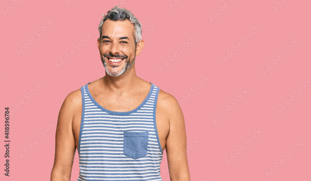 Middle age grey-haired man wearing casual style with sleeveless shirt looking positive and happy standing and smiling with a confident smile showing teeth Middle age grey-haired man wearing casual style with sleeveless shirt looking positive and happy standing and smiling with a confident smile showing teeth