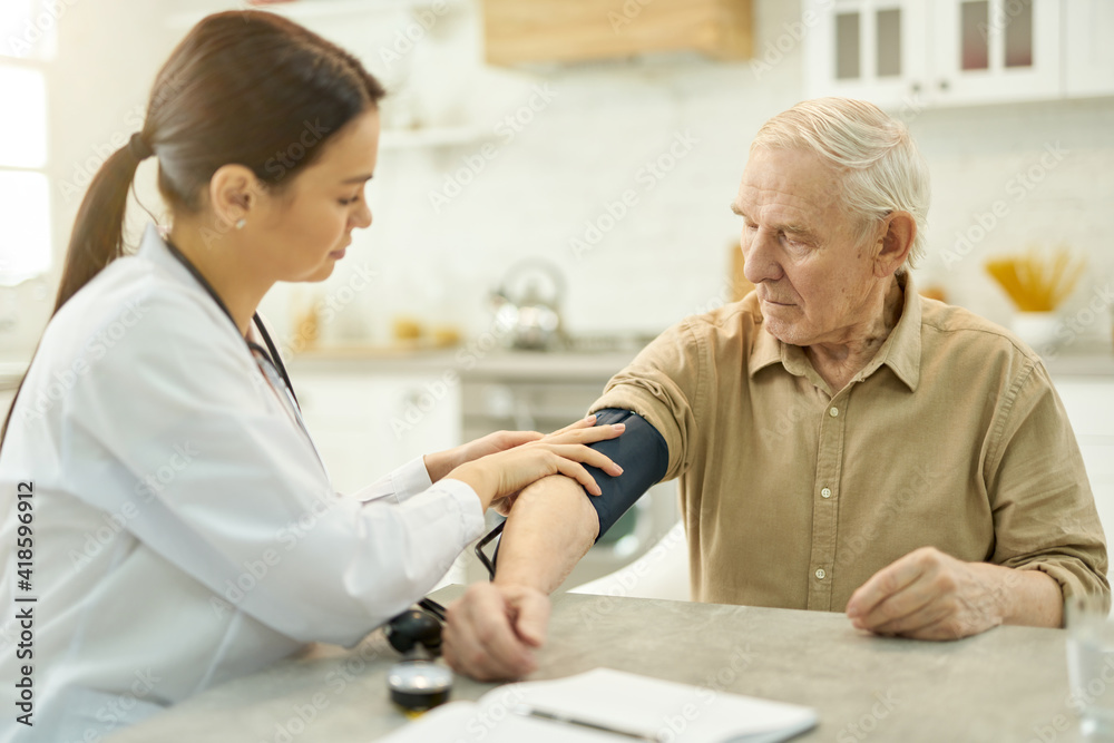 Fototapeta premium Attentive medic preparing to measure elderly man blood pressure