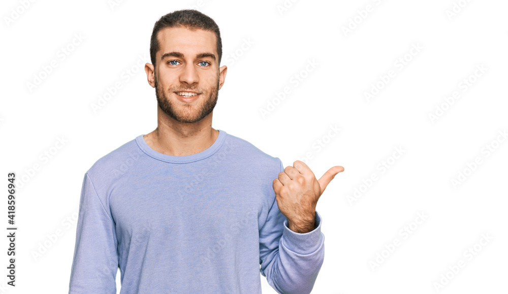 Young caucasian man wearing casual clothes smiling with happy face looking and pointing to the side with thumb up. Young caucasian man wearing casual clothes smiling with happy face looking and pointing to the side with thumb up.