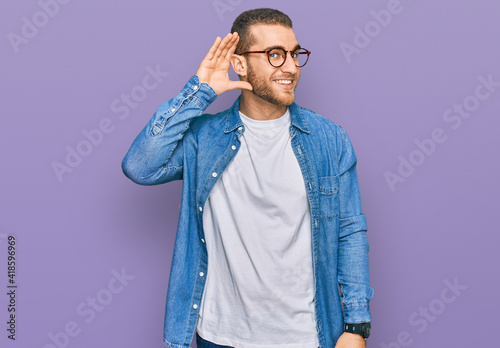 Young caucasian man wearing casual clothes smiling with hand over ear listening an hearing to rumor or gossip. deafness concept. © Krakenimages.com
