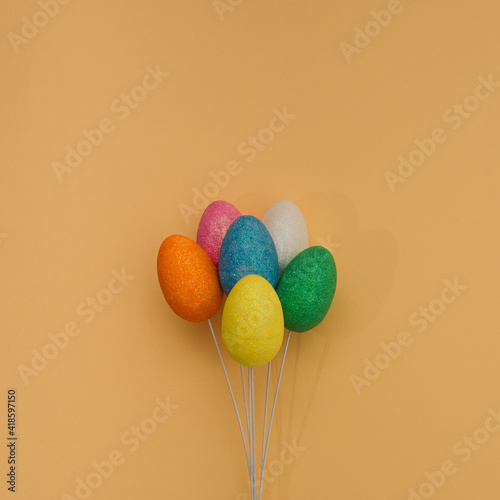 Yellow, white, pink, green, orange and blue egg on the wire look like balloons. Flat lay on orange background.