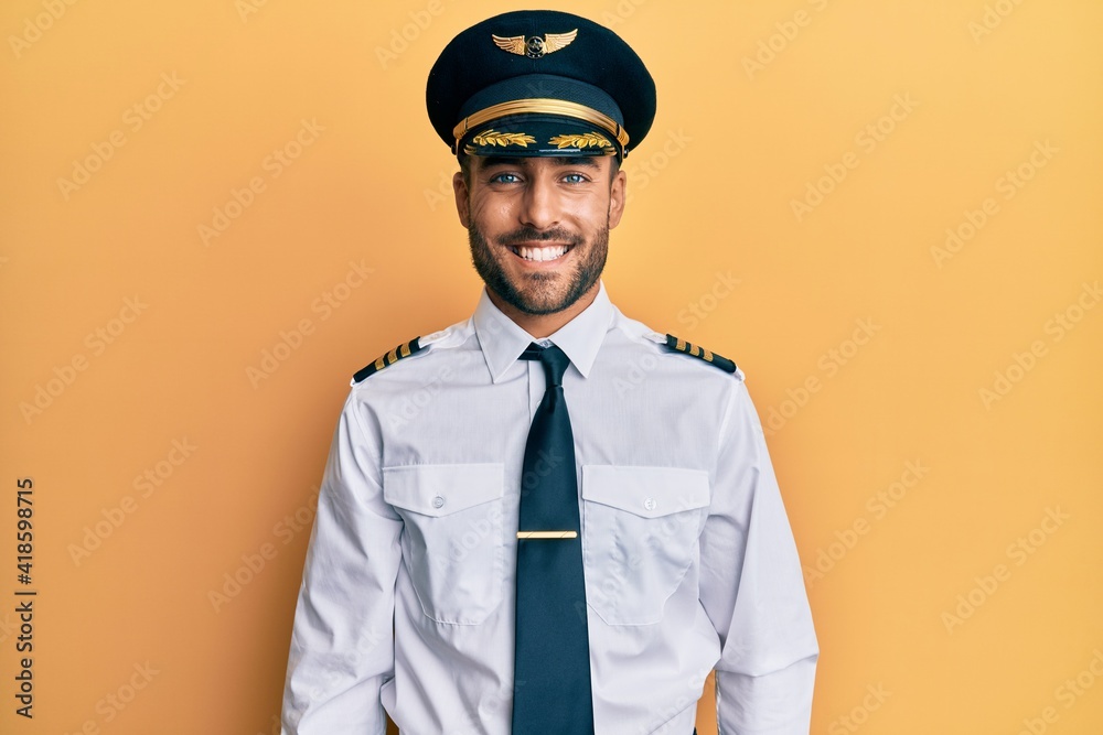Handsome hispanic man wearing airplane pilot uniform with a happy and cool smile on face. lucky person. - obrazy, fototapety, plakaty 
