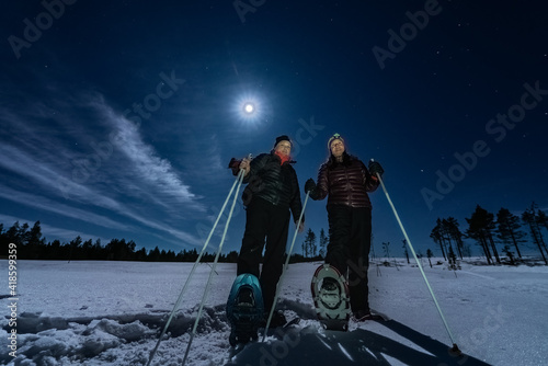 Tableau sur toile Beautiful middle aged men and women in snowshoes stand in night rare snowy winter forest under full moon light