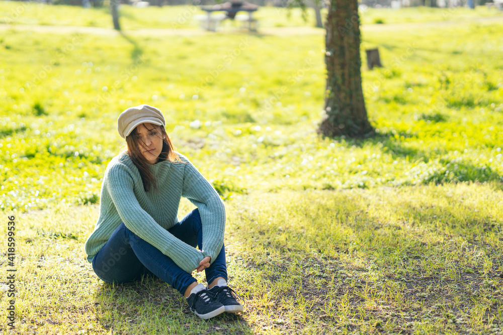 beautiful woman in cap sitting in a park enjoying a fresh spring afternoon in the sun. Lifestyle
