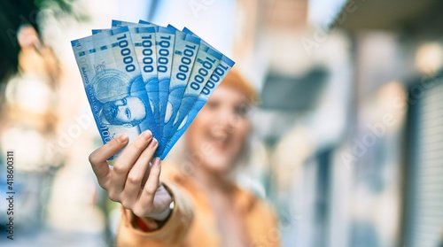 Foto Young blonde girl smiling happy holding chilean pesos banknotes at the city