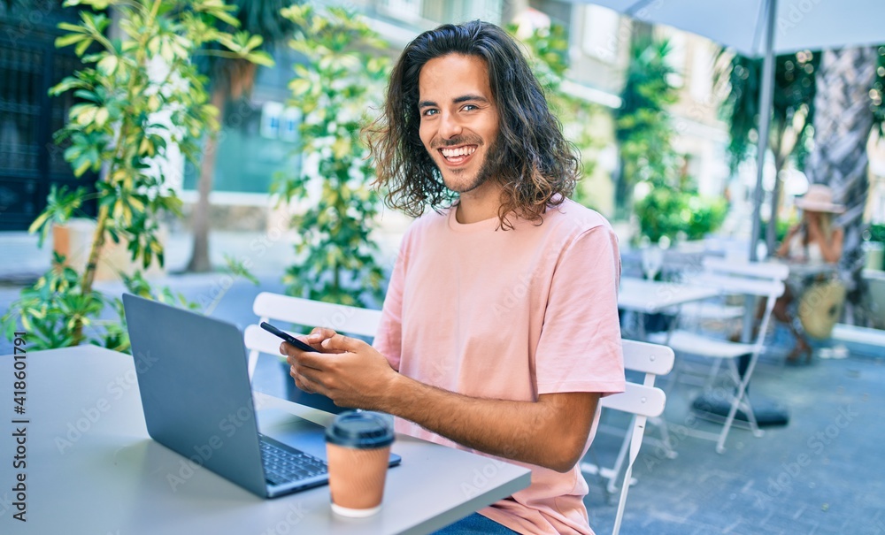 Young hispanic man smiling happy working using laptop and smartphone at terrace of coffee shop. Young hispanic man smiling happy working using laptop and smartphone at terrace of coffee shop.