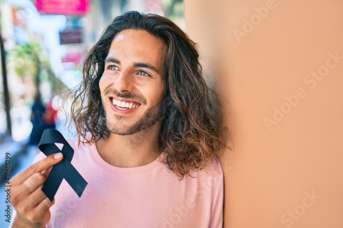 Young hispanic man smiling happy holding mouring black ribbon leaning on the wall. photo