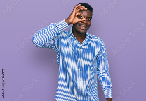 Handsome business black man wearing casual striped t shirt smiling happy doing ok sign with hand on eye looking through fingers