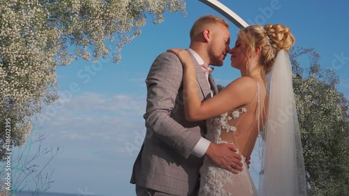The bride and groom kiss against the background of the arch and the blue sky. Close up