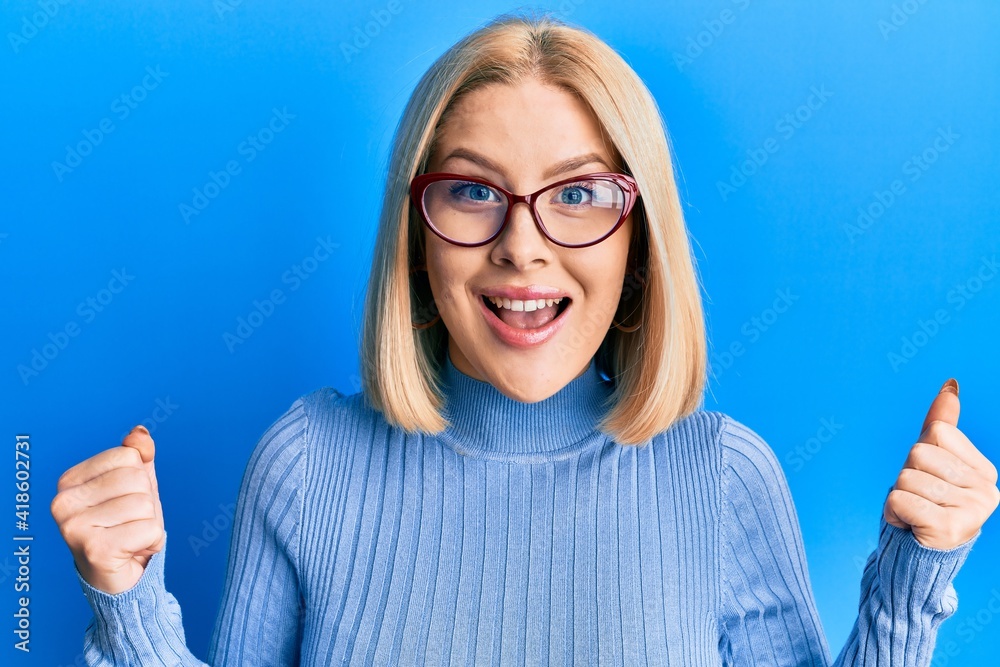 Young blonde woman wearing casual clothes and glasses celebrating surprised and amazed for success with arms raised and open eyes. winner concept. Young blonde woman wearing casual clothes and glasses celebrating surprised and amazed for success with arms raised and open eyes. winner concept.