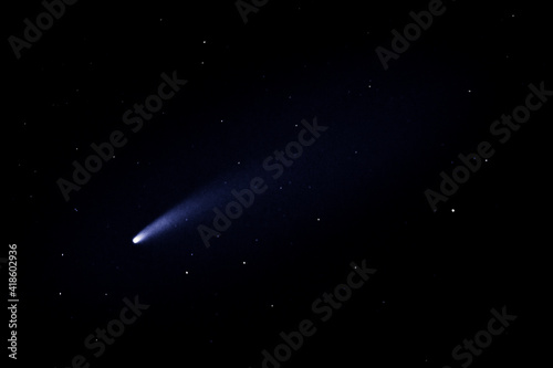 Comet Neowise flies past the earth, viewed from below into the dark sky.