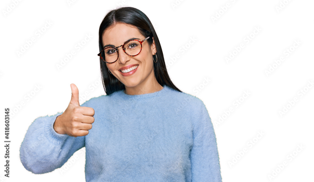 Young hispanic woman wearing casual clothes and glasses doing happy thumbs up gesture with hand. approving expression looking at the camera showing success. Young hispanic woman wearing casual clothes and glasses doing happy thumbs up gesture with hand. approving expression looking at the camera showing success.