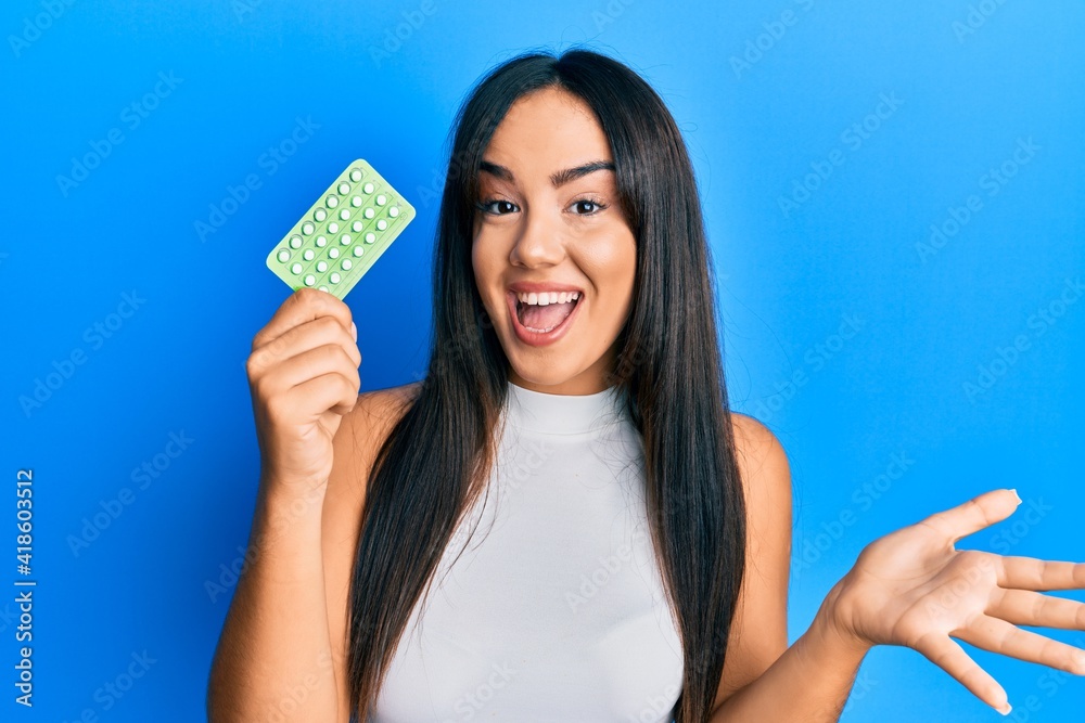 Young beautiful hispanic girl holding birth control pills celebrating achievement with happy smile and winner expression with raised hand Young beautiful hispanic girl holding birth control pills celebrating achievement with happy smile and winner expression with raised hand