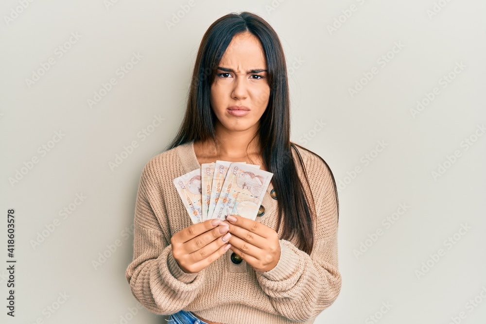 Young beautiful hispanic girl holding 10 united kingdom pounds banknotes skeptic and nervous, frowning upset because of problem. negative person. Young beautiful hispanic girl holding 10 united kingdom pounds banknotes skeptic and nervous, frowning upset because of problem. negative person.