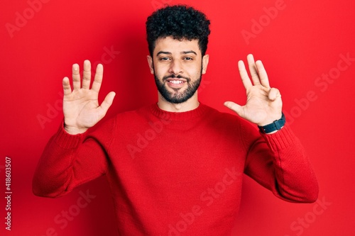 Young arab man with beard wearing casual red sweater showing and pointing up with fingers number nine while smiling confident and happy.