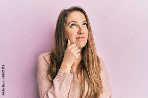 Young blonde woman wearing casual sweater serious face thinking about question with hand on chin, thoughtful about confusing idea