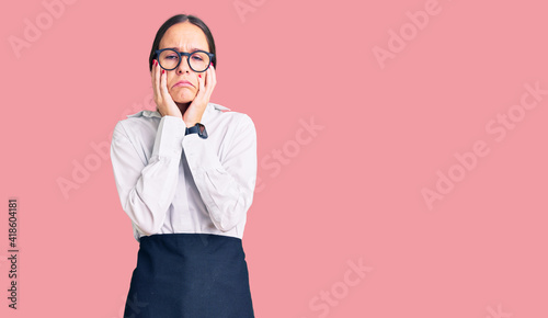 Beautiful brunette young woman wearing professional waitress apron tired hands covering face, depression and sadness, upset and irritated for problem