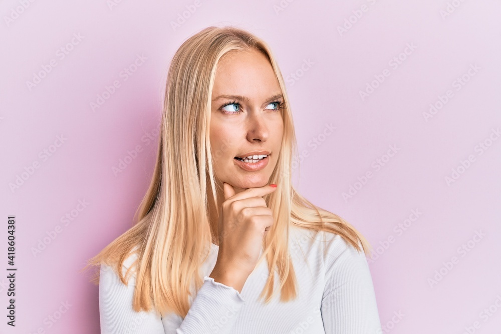 Young blonde girl wearing casual clothes with hand on chin thinking about question, pensive expression. smiling with thoughtful face. doubt concept. Young blonde girl wearing casual clothes with hand on chin thinking about question, pensive expression. smiling with thoughtful face. doubt concept.