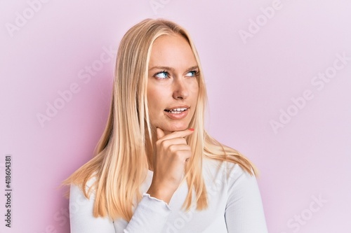 Young blonde girl wearing casual clothes with hand on chin thinking about question, pensive expression. smiling with thoughtful face. doubt concept.