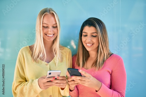 Two beautiful and young girl friends together having fun at the city using smartphone