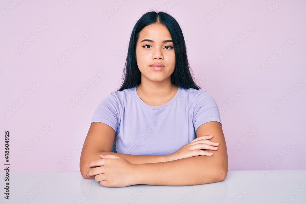 Young beautiful asian girl wearing casual clothes sitting on the table with serious expression on face. simple and natural looking at the camera. Young beautiful asian girl wearing casual clothes sitting on the table with serious expression on face. simple and natural looking at the camera.