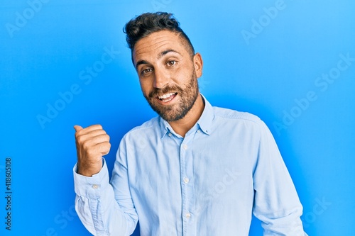 Handsome man with beard wearing casual clothes smiling with happy face looking and pointing to the side with thumb up.