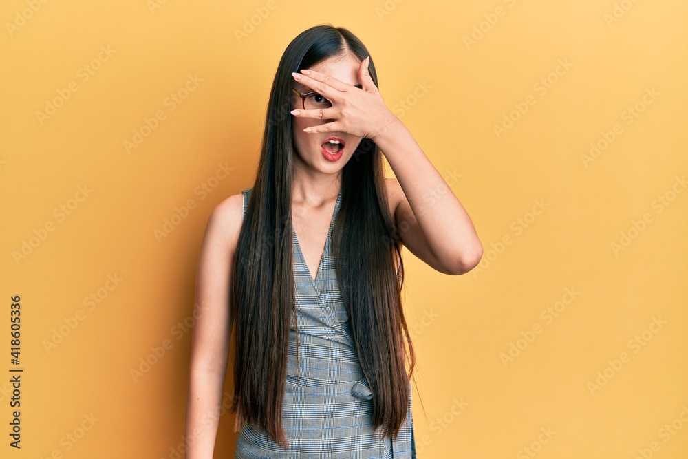 Young chinese woman wearing business dress and glasses peeking in shock covering face and eyes with hand, looking through fingers afraid