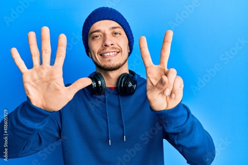 Hispanic young man wearing sweatshirt and headphones showing and pointing up with fingers number seven while smiling confident and happy.