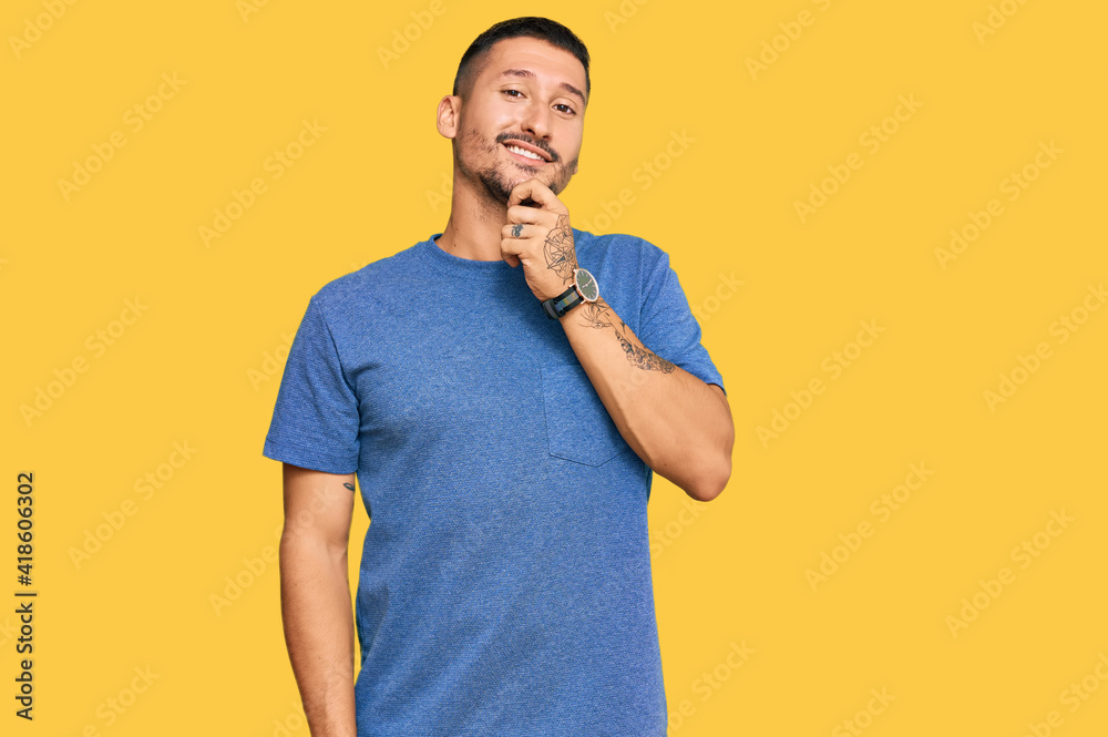 Handsome man with tattoos wearing casual clothes looking confident at the camera with smile with crossed arms and hand raised on chin. thinking positive. Handsome man with tattoos wearing casual clothes looking confident at the camera with smile with crossed arms and hand raised on chin. thinking positive.
