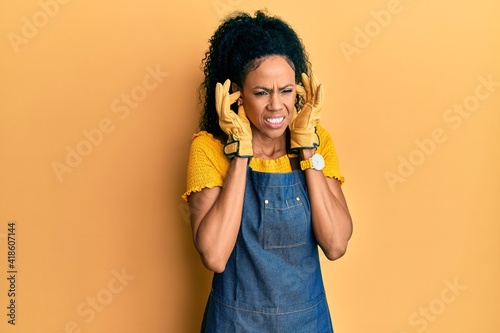 Middle age african american woman wearing professional apron covering ears with fingers with annoyed expression for the noise of loud music. deaf concept.