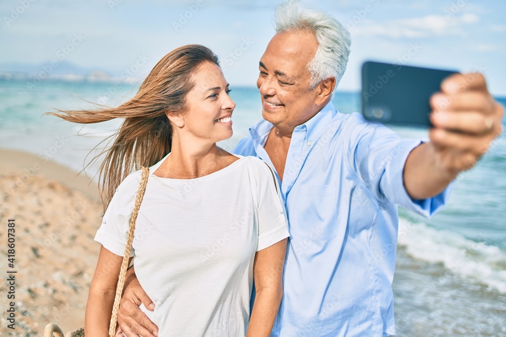 Middle age hispanic couple smiling happy making selfie by the smartphone at the beach.