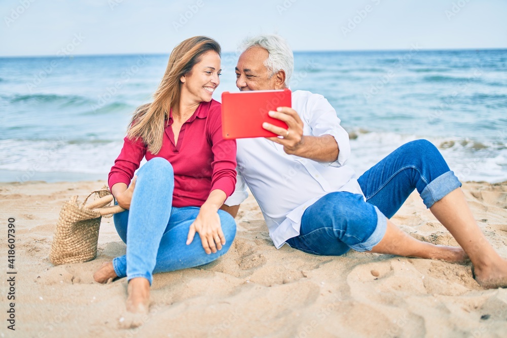 Middle age hispanic couple smiling happy making selfie by the tablet at the beach. Middle age hispanic couple smiling happy making selfie by the tablet at the beach.