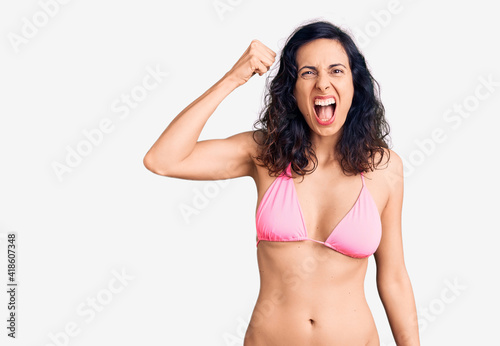 Young beautiful hispanic woman wearing bikini angry and mad raising fist frustrated and furious while shouting with anger. rage and aggressive concept. © Krakenimages.com
