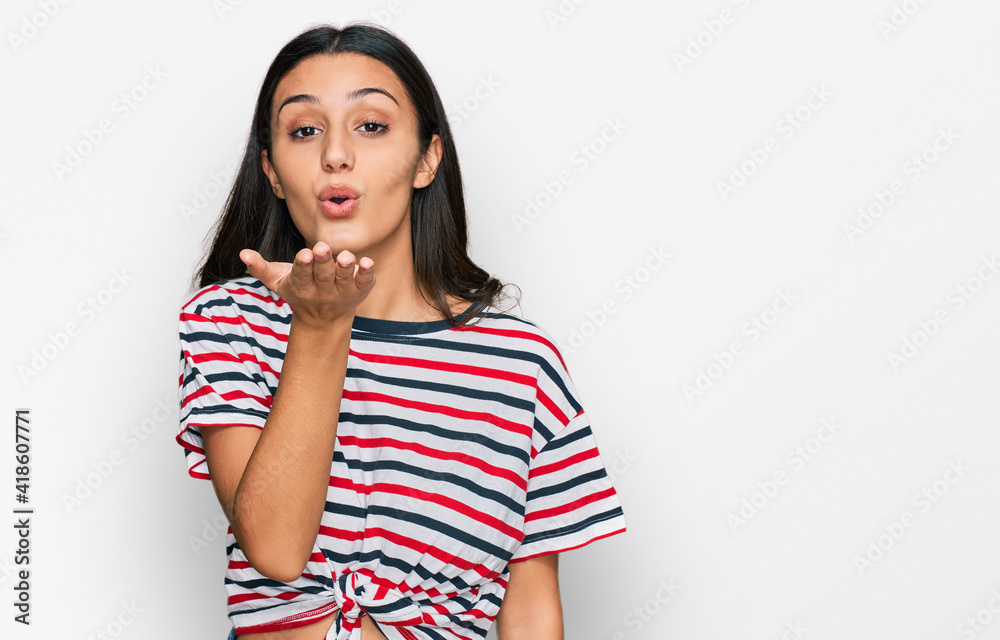 Young hispanic girl wearing casual clothes looking at the camera blowing a kiss with hand on air being lovely and sexy. love expression. Young hispanic girl wearing casual clothes looking at the camera blowing a kiss with hand on air being lovely and sexy. love expression.