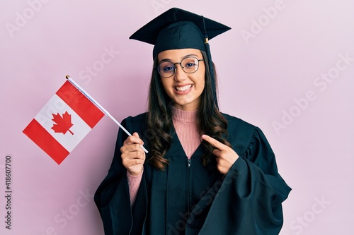 Young hispanic woman wearing graduation uniform holding canada flag smiling happy pointing with hand and finger